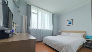 Habitación de hotel con cama, escritorio con televisor, ventana con cortinas e imagen en la pared.