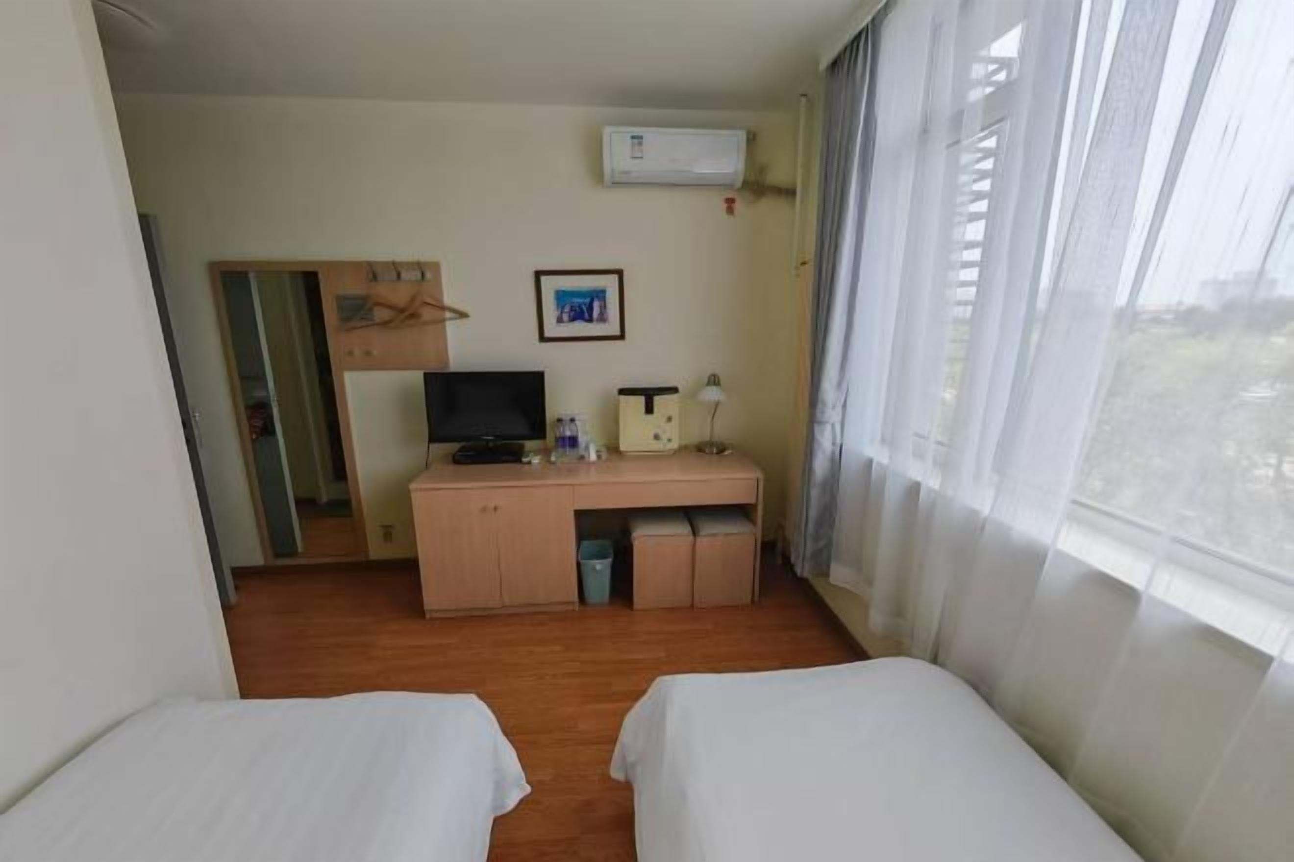 A hotel room with two beds, a desk with a computer, a TV, and a window with curtains.