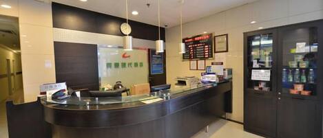 A hotel reception area with a curved counter, a digital display board, and a glass partition.