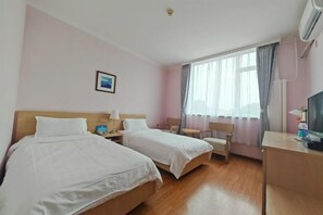 Hotellihuone, jossa on kaksi sänkyä, työpöytä, tuoli, televisio ja ikkuna, jossa on verhot.