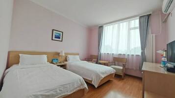 Una habitación de hotel con dos camas, un escritorio, una silla, un televisor y una ventana con cortinas.