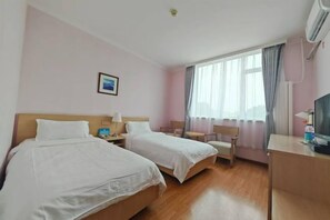Una habitación de hotel con dos camas, un escritorio, una silla, un televisor y una ventana con cortinas.
