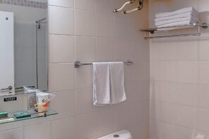 Kylpyhuone, jossa on lasinen suihkuseinä, pyyheteline, jossa on siististi taitettu pyyhe, lasihylly, jossa on hygieniatuotteita, ja wc-istuin.