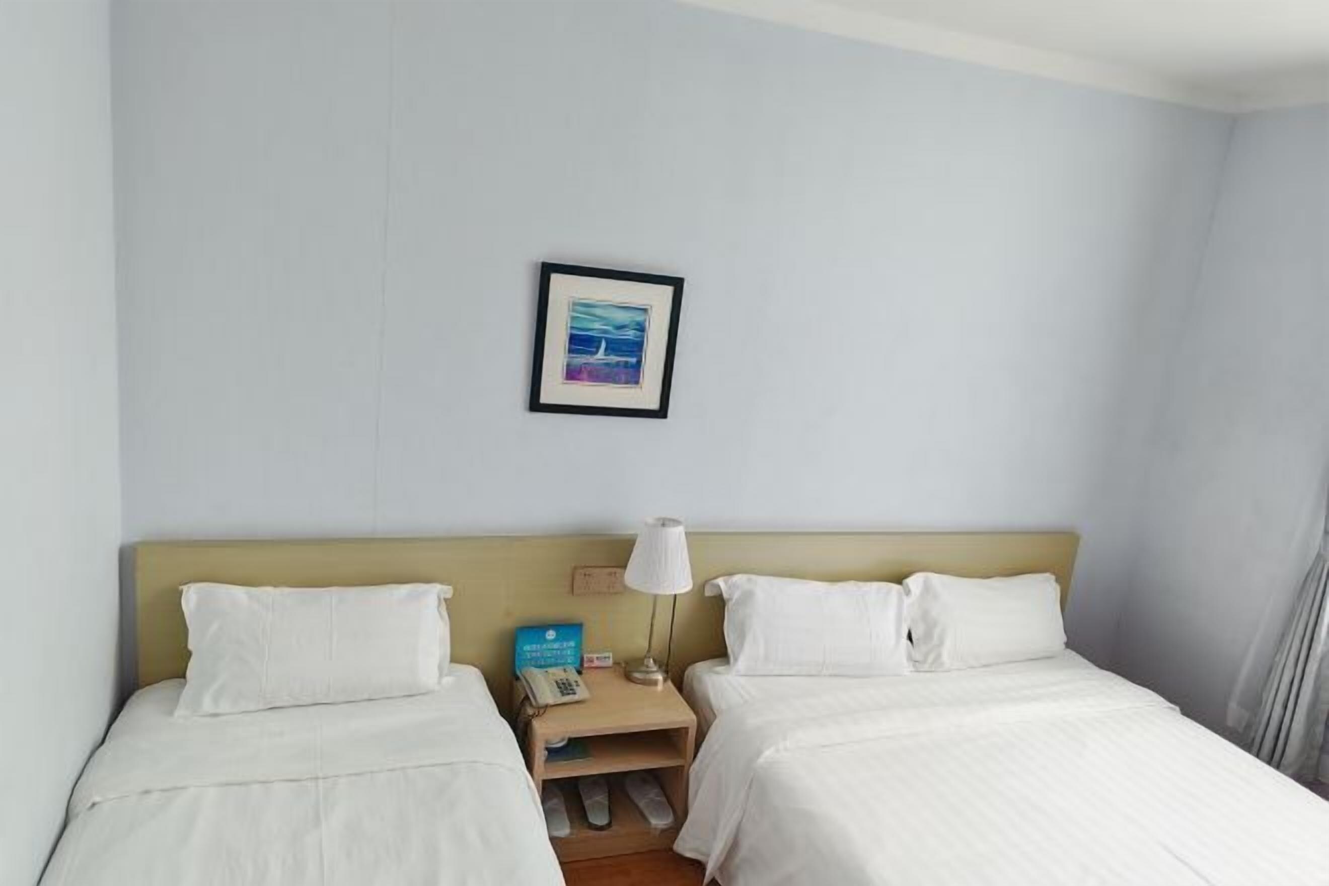 Habitación de hotel con dos camas, una mesita de noche con lámpara, un cuadro enmarcado en la pared y una pequeña mesa con teléfono.