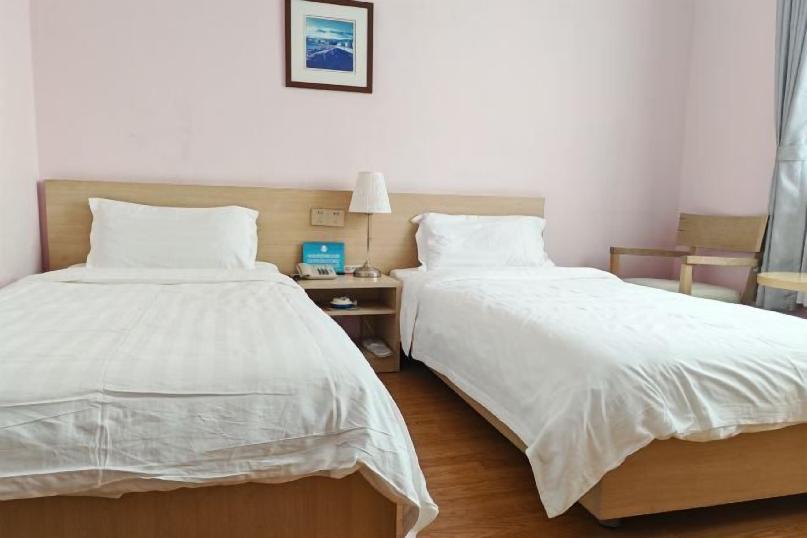 Ein Hotelzimmer mit zwei Einzelbetten, einem Nachttisch mit Lampe, einem Sessel und einem gerahmten Bild an der Wand.