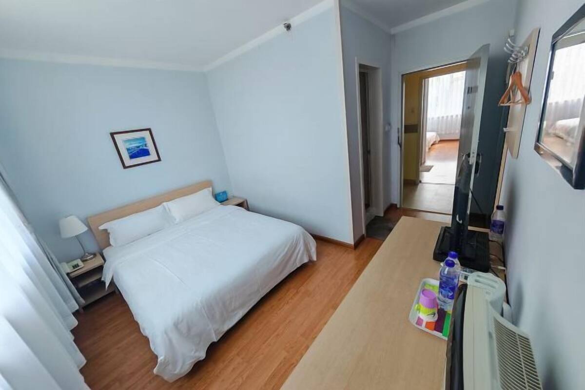 A hotel room with a bed, a nightstand, a lamp, a picture on the wall, a mirror, and a window.