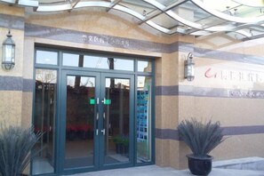 A building entrance with glass doors, a sign above indicating a specific room number, and a wall-mounted light fixture. - Guantong Modern Hotel (Beijing Qianmen) (Beijing)