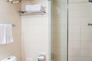 Een badkamer met een douchecabine van glas, een toilet en een handdoekrek met opgevouwen handdoeken.