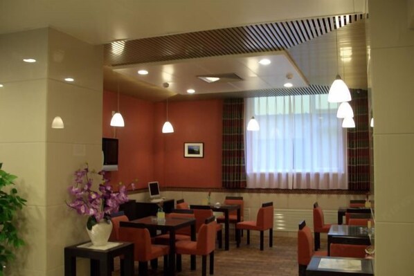 A hotel dining area with tables and chairs, pendant lights, a television, and a window with curtains. - Guantong Modern Hotel (Beijing Qianmen) (Beijing)