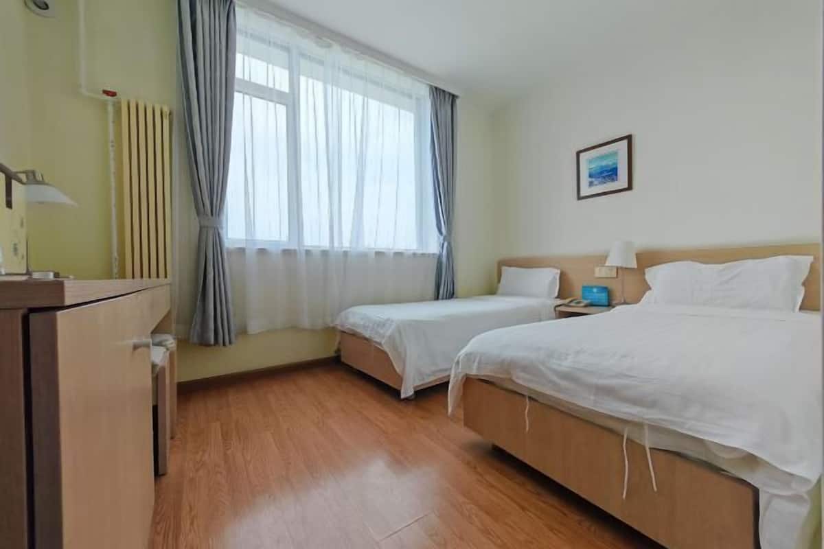 A hotel room with two beds, a desk, a lamp, a picture on the wall, and a window with curtains.