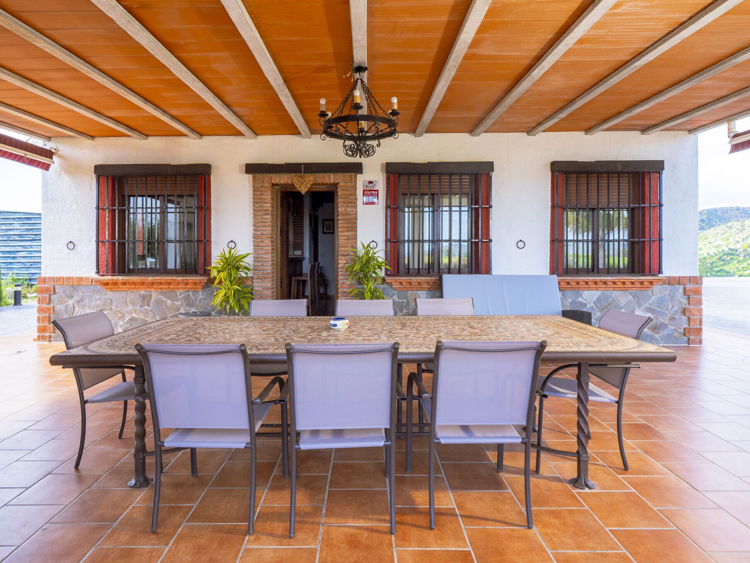 Un patio cubierto con una mesa grande y sillas, paredes de piedra y techo de madera.