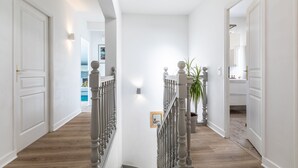 A hallway with a wooden floor, white walls, and a staircase with a balustrade.