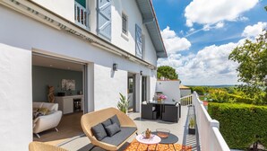 A modern outdoor patio with wicker furniture and a patterned rug, overlooking a lush garden and a scenic landscape.