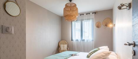 A bedroom with a bed, a chair, a window with curtains, and a wall-mounted light fixture.