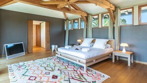 A bedroom with a wooden ceiling, a bed, a TV, and a colorful rug.