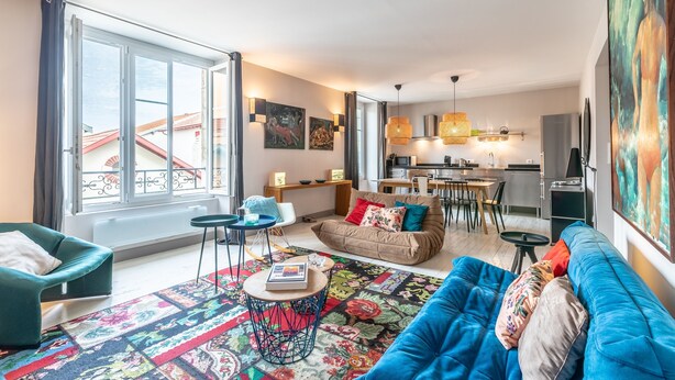 A modern living room with a sofa, a coffee table, and a dining area. - Romy - En centre-ville (Biarritz)
