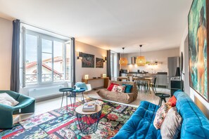 A modern living room with a sofa, a coffee table, and a dining area. - Romy - En centre-ville (Biarritz)