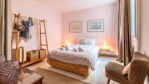 A bedroom with a wooden bed, a hanging chair, a small table, and a wardrobe with hanging clothes and baskets. - Romy - En centre-ville (Biarritz)