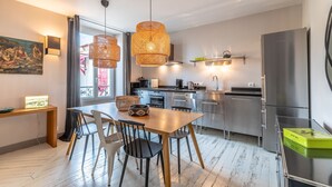 A modern kitchen with a dining area, featuring a wooden table, chairs, and a hanging light fixture. - Romy - En centre-ville (Biarritz)