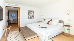 A modern bedroom with a large bed, bedside tables, a bench, and a painting on the wall. - Sunset - Vue exceptionnelle sur l'océan (Biarritz)