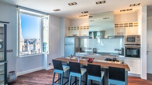 A modern kitchen with a large window, built-in appliances, and a central island with bar stools. - Atalaye - Grand appartement vue mer (Biarritz)
