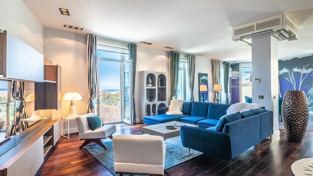 A modern living room with a blue sofa, a white armchair, and a coffee table. There is a large window with curtains, a flat-screen TV, and a decorative vase. - Atalaye - Grand appartement vue mer (Biarritz)