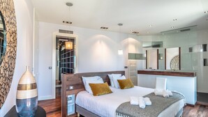 A modern hotel room with a large bed, a bedside table, a mirror, and a bathroom with a glass partition. - Atalaye - Grand appartement vue mer (Biarritz)