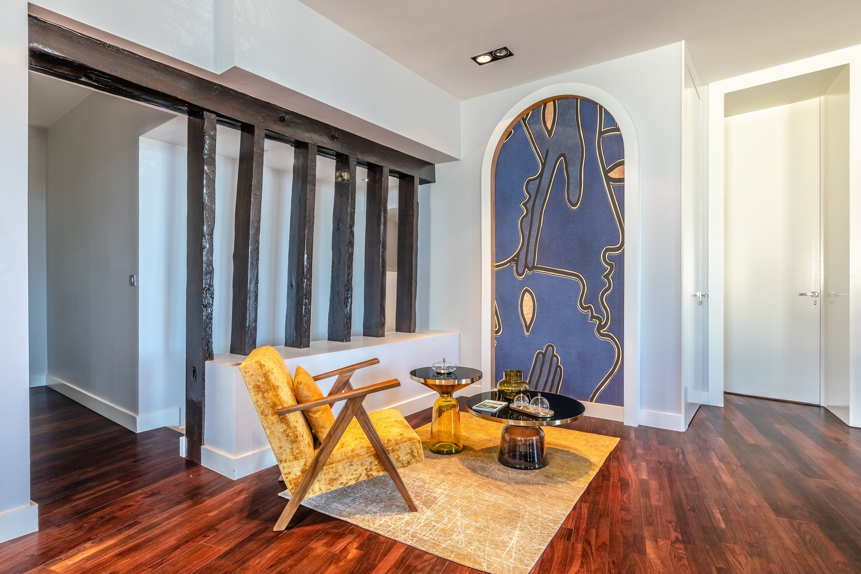 A modern living room with a dark wood floor, a yellow sofa, a coffee table, and a unique wall art piece.