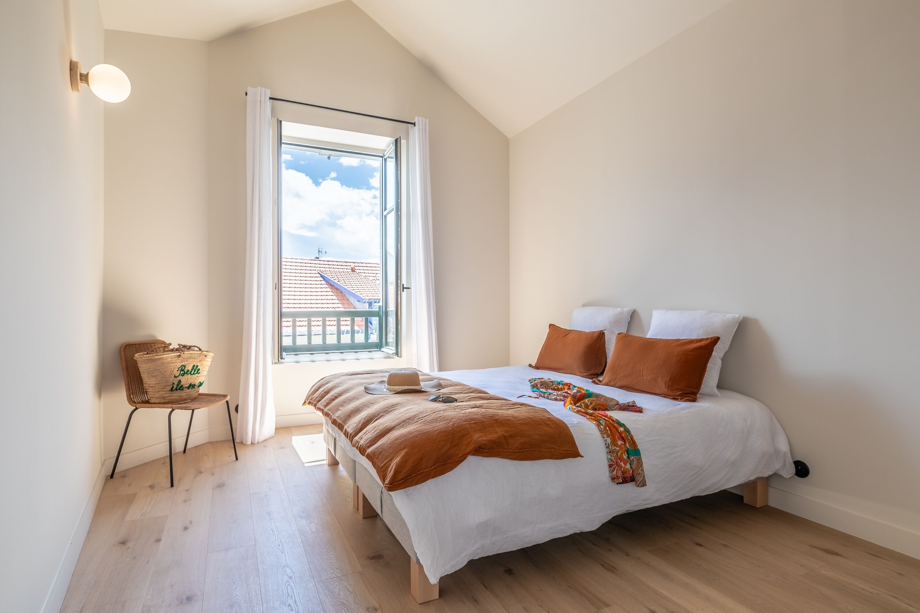 Ein Schlafzimmer mit einem großen Bett, einem Fenster mit Blick auf ein Gebäude, einem Stuhl und einem Korb.