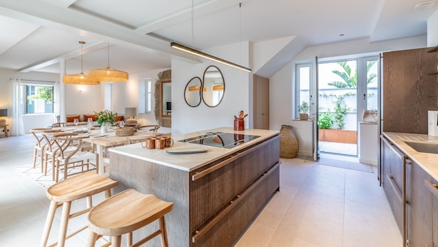 Une cuisine spacieuse dotée d’un grand îlot central, de tabourets de bar en bois et offrant une vue sur l’extérieur.