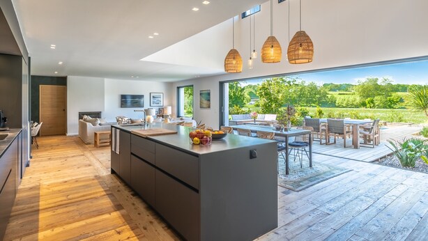 A modern kitchen with a large island, wooden flooring, and pendant lighting. - Villa Loreteian - Splendide villa au calme (Ahetze)