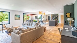A spacious living area with a sofa, chairs, and a dining table. There is a kitchen area in the background with a staircase leading to another level. - Villa Loreteian - Splendide villa au calme (Ahetze)