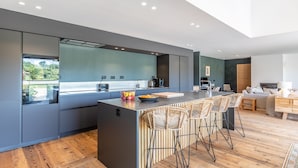 A modern kitchen with a central island, bar stools, and a dining area with a sofa and table. - Villa Loreteian - Splendide villa au calme (Ahetze)