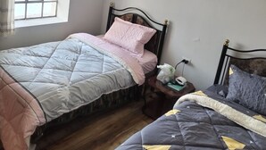 A bedroom with two beds, a window with curtains, a wooden floor, and a ceiling light fixture. - Room 5 (Huancayo)