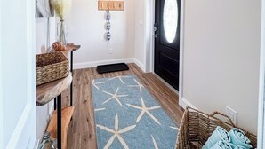 A hallway with a wooden floor, a star-patterned rug, a woven basket with towels, and a door with a frosted glass window. - Pet Friendly 2bed/2bath coastal hideaway (Jensen Beach)