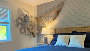 A bedroom with a large bed, a decorative wall hanging, a lamp, and a window with blinds. - Pet Friendly 2bed/2bath coastal hideaway (Jensen Beach)