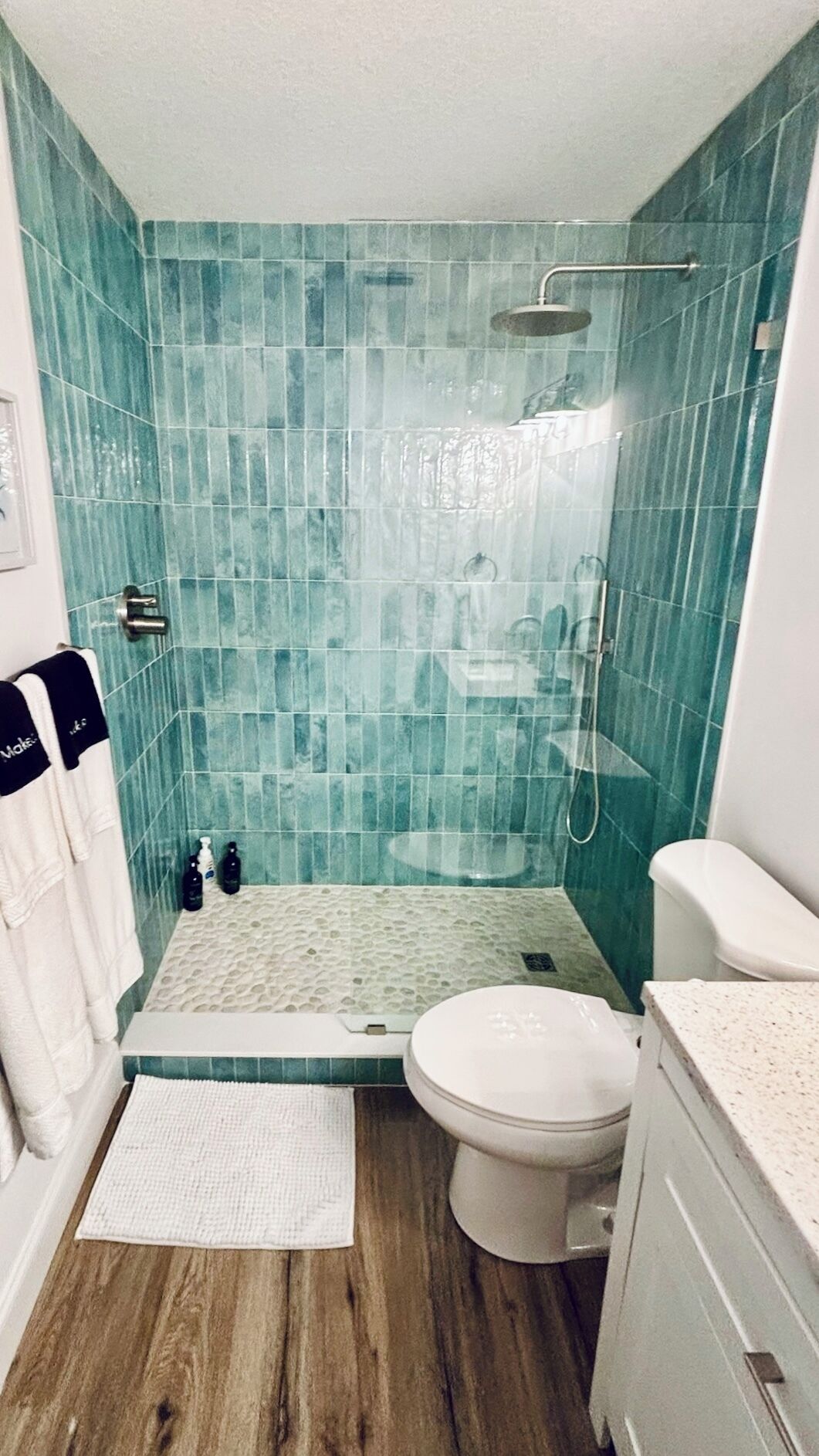A bathroom with teal mosaic tiles, a shower, a toilet, and a sink.