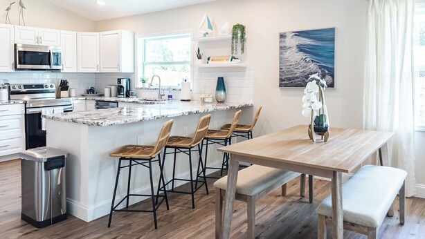 A modern kitchen with white cabinetry, a granite countertop, and a wooden dining table with four chairs. - Pet Friendly 2bed/2bath coastal hideaway (Jensen Beach)