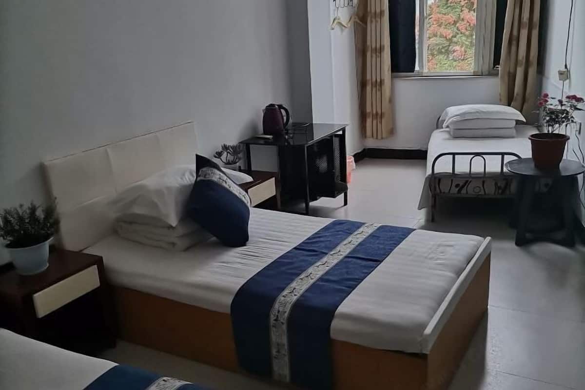 Un dormitorio con cama, mesitas de noche, una ventana con cortinas y una planta en maceta.