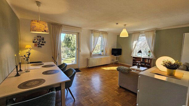 A spacious living area with a dining table, chairs, a sofa, and a TV. - Garden apartment with terrace (Kassel)
