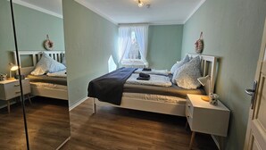 A bedroom with a bed, nightstands, a mirror, and a window with curtains. - Garden apartment with terrace (Kassel)