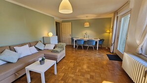 A living room with a sofa, a dining table with chairs, a small table with a plant, and a radiator. - Garden apartment with terrace (Kassel)