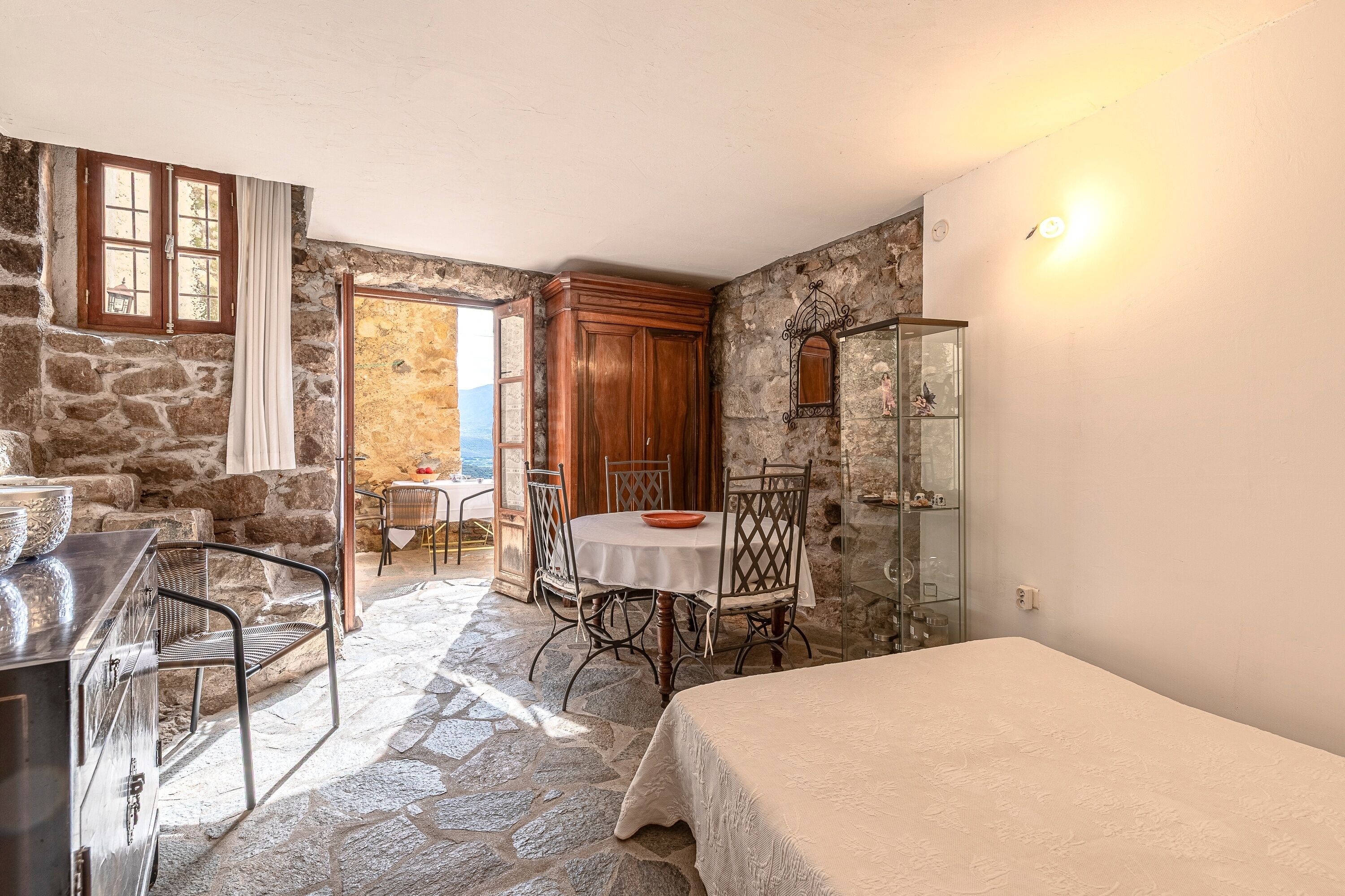 Une pièce aux murs de pierre, avec un lit, une table et des chaises, et un meuble en bois.