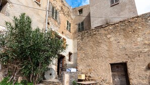 Une ruelle étroite bordée d’immeubles en pierre, avec une porte en bois et une table sur laquelle se trouve une boîte.