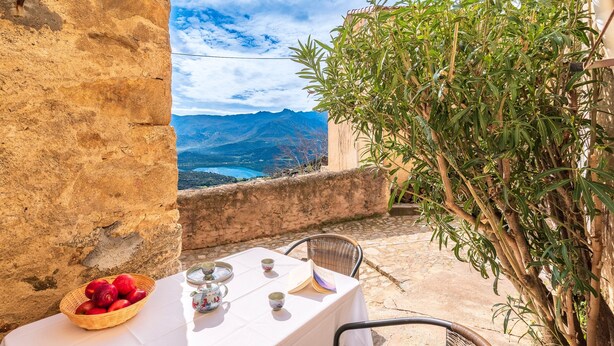 Une table dressée avec un panier de fruits, des tasses à thé et un livre, offrant une vue panoramique sur les montagnes.