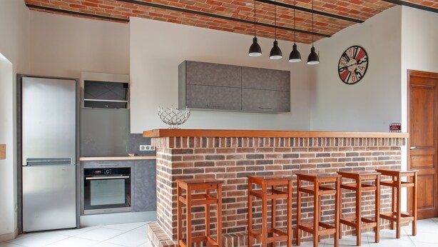 A kitchen with a brick wall, stainless steel appliances, and wooden bar stools. - Le Cheval Blanc - Proche Amiens, grand jardin (Damery)