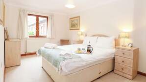 A neatly arranged bedroom with a bed, bedside tables, a radiator, a window with curtains, and a framed picture on the wall. - Sycamore (Dereham)