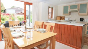 A kitchen with wooden cabinets, a central island, and a dining area with chairs and a table set for four. - Sycamore (Dereham)