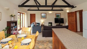A dining area with a wooden table set for breakfast, a sofa, and a TV in the background.