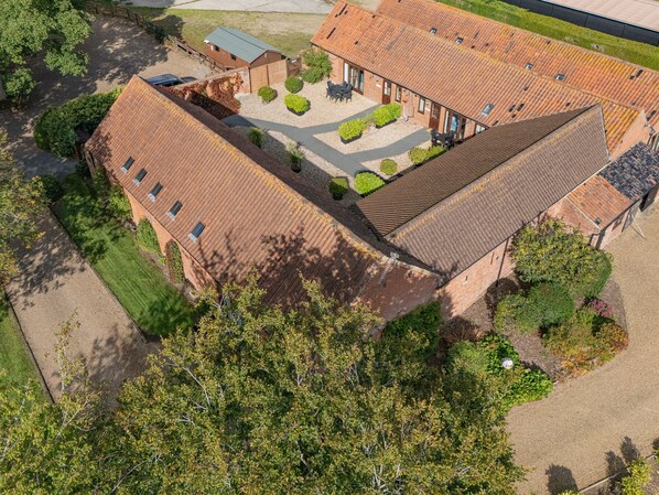 Vue aérienne d’un bâtiment doté d’un toit en pente, entouré de verdure et d’une cour dallée.